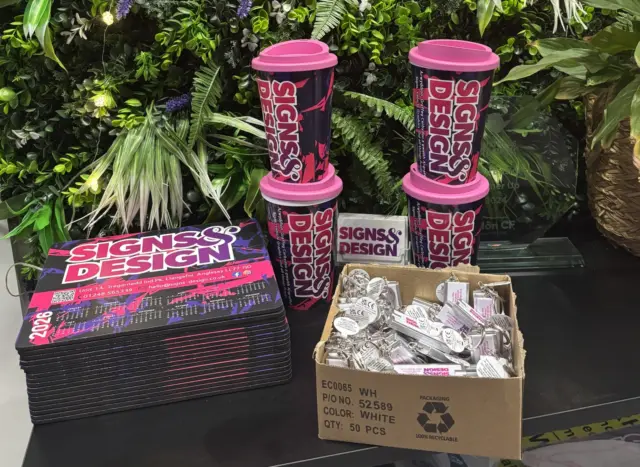 Display of Signs & Design branded promotional merchandise including printed reusable cups, business cards and keyrings at an exhibition stand
